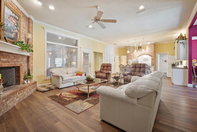 living room with hardwood / wood-style flooring, ornamental molding, ceiling fan, a brick fireplace, and a textured ceiling