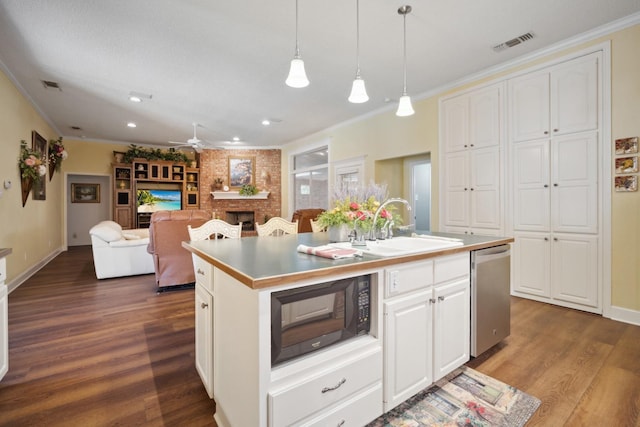 kitchen with hanging light fixtures, a brick fireplace, dishwasher, an island with sink, and white cabinets