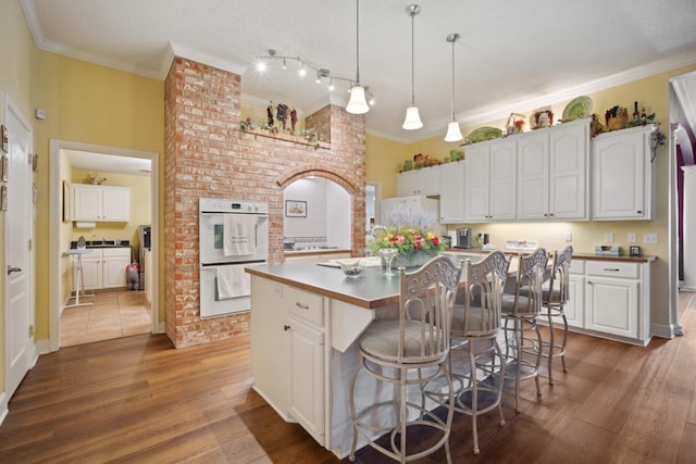 kitchen featuring crown molding, white appliances, hardwood / wood-style flooring, a center island, and white cabinets