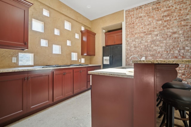 kitchen featuring sink, a breakfast bar, black refrigerator with ice dispenser, and decorative backsplash