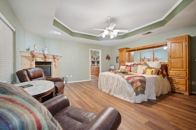 bedroom with a fireplace, ceiling fan, light hardwood / wood-style floors, a raised ceiling, and crown molding