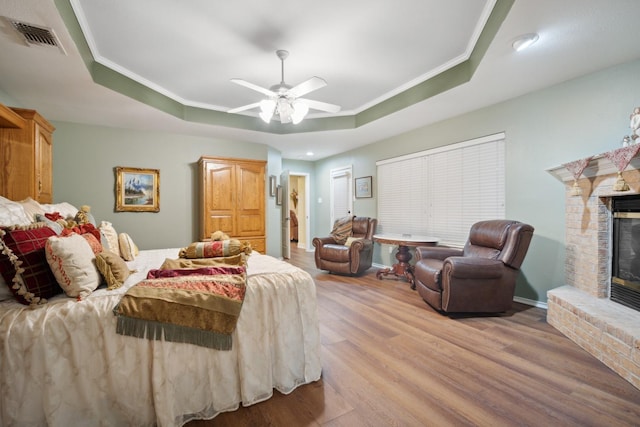 bedroom featuring crown molding, a brick fireplace, a tray ceiling, and light hardwood / wood-style floors