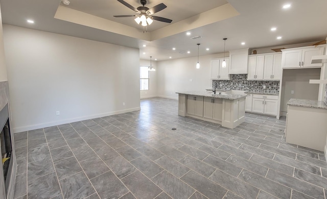 kitchen featuring a kitchen island with sink, light stone counters, a tray ceiling, and white cabinets