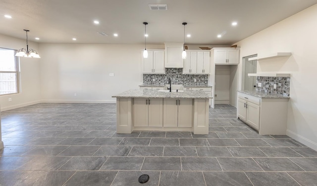 kitchen featuring sink, white cabinetry, hanging light fixtures, a kitchen island with sink, and light stone countertops