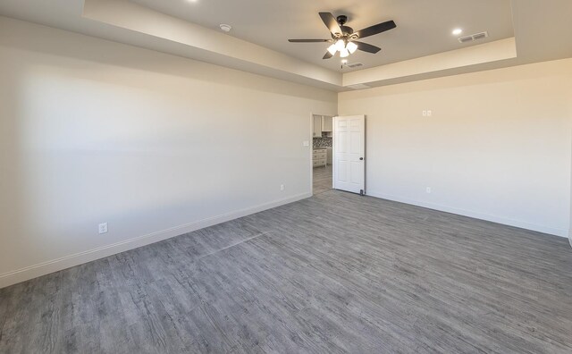 unfurnished room featuring a raised ceiling, hardwood / wood-style floors, and ceiling fan