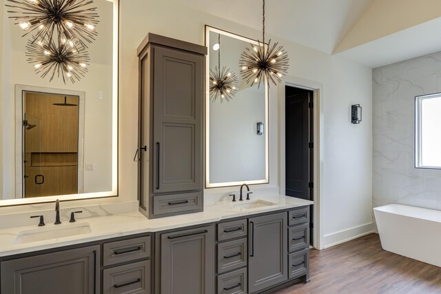 7710 46th St, Lubbock, TX 79407 - bathroom featuring a chandelier, double vanity, a freestanding tub, wood finished floors, and vaulted ceiling