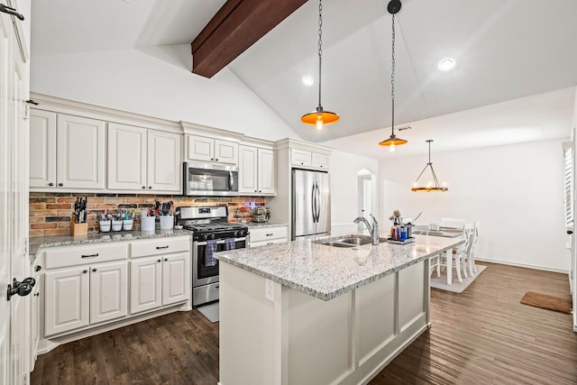 kitchen featuring appliances with stainless steel finishes, a sink, beam ceiling, an island with sink, and backsplash