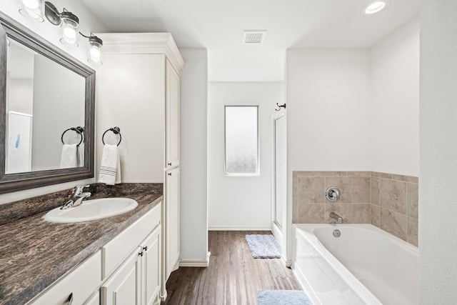 full bath with vanity, wood finished floors, a garden tub, and baseboards