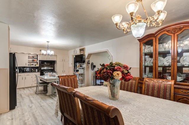 dining area with a notable chandelier, a textured ceiling, and light wood-type flooring