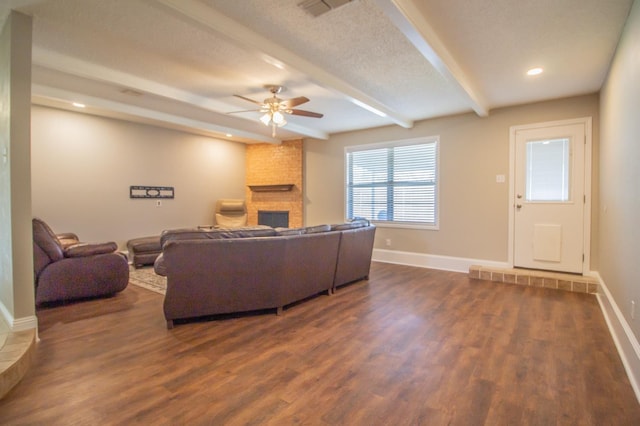 living room featuring ceiling fan, dark wood-type flooring, a large fireplace, and beamed ceiling