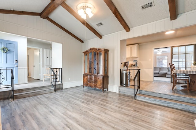 living room featuring vaulted ceiling with beams, a textured ceiling, and light wood-type flooring