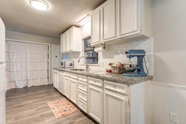 kitchen with sink, light stone counters, white cabinetry, light hardwood / wood-style flooring, and white dishwasher