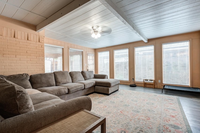 living room with beam ceiling, wood-type flooring, ceiling fan, and brick wall