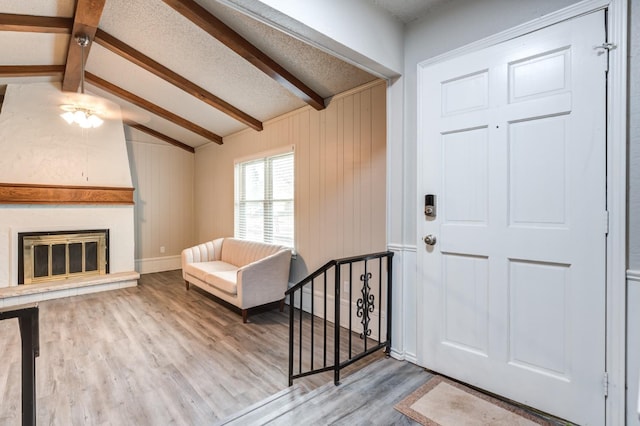 entryway featuring wooden walls, lofted ceiling with beams, a large fireplace, hardwood / wood-style flooring, and a textured ceiling