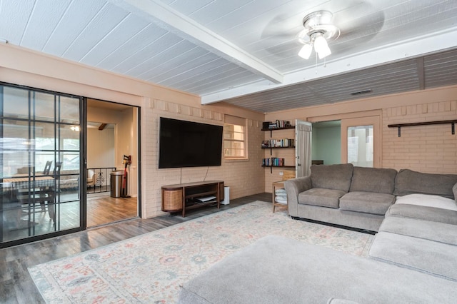 living room featuring beam ceiling, hardwood / wood-style flooring, ceiling fan, and brick wall