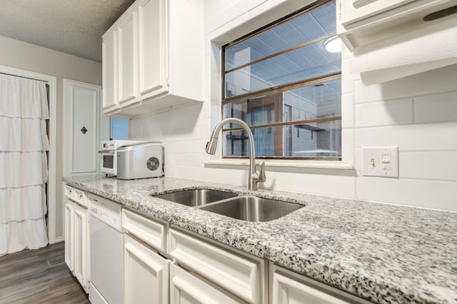 kitchen featuring white dishwasher, sink, white cabinetry, and light stone counters