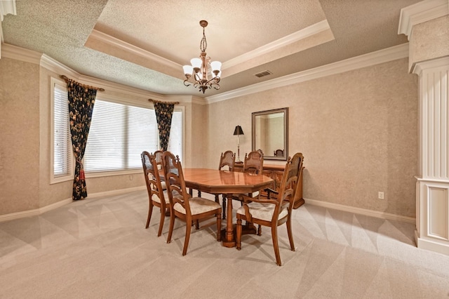 dining area featuring ornamental molding, light colored carpet, a raised ceiling, a chandelier, and ornate columns