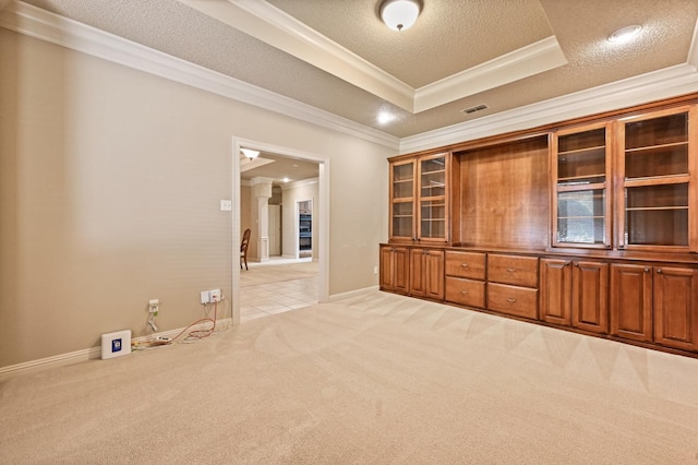 interior space with crown molding, a textured ceiling, a tray ceiling, light colored carpet, and decorative columns