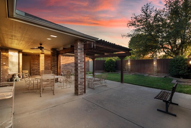 patio terrace at dusk featuring a yard and ceiling fan