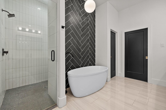 full bathroom with a freestanding bath, a shower stall, baseboards, and tile walls