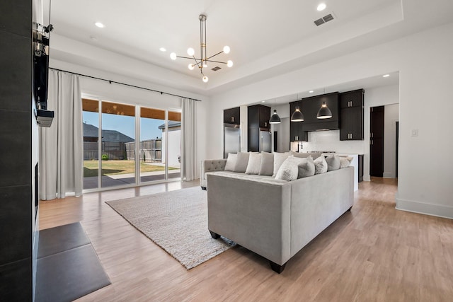 living room with an inviting chandelier, light wood finished floors, visible vents, and a raised ceiling