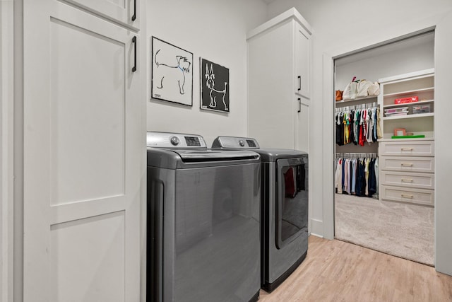 clothes washing area with separate washer and dryer, light wood-type flooring, and cabinet space