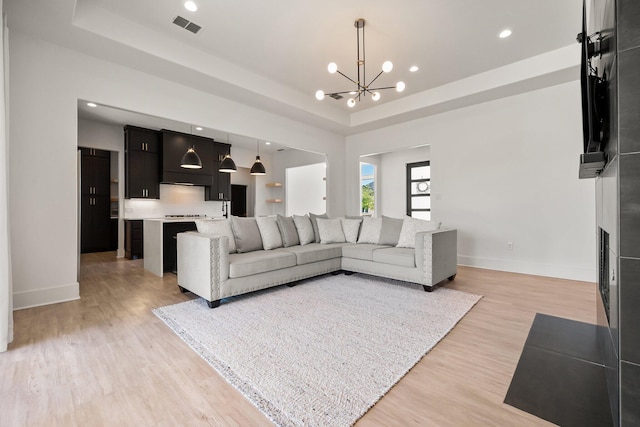 living area with baseboards, a notable chandelier, a tray ceiling, and visible vents
