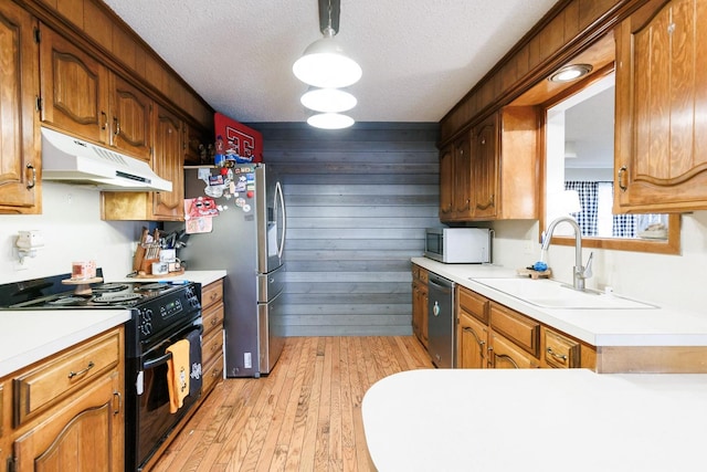 kitchen with sink, light hardwood / wood-style flooring, appliances with stainless steel finishes, a textured ceiling, and wood walls