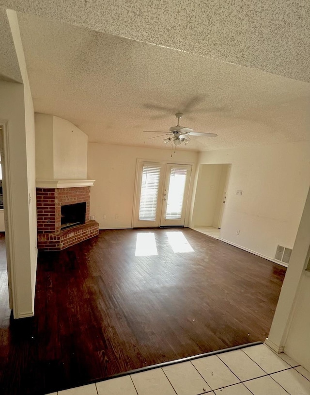 unfurnished living room with light tile patterned flooring, a brick fireplace, a textured ceiling, and ceiling fan