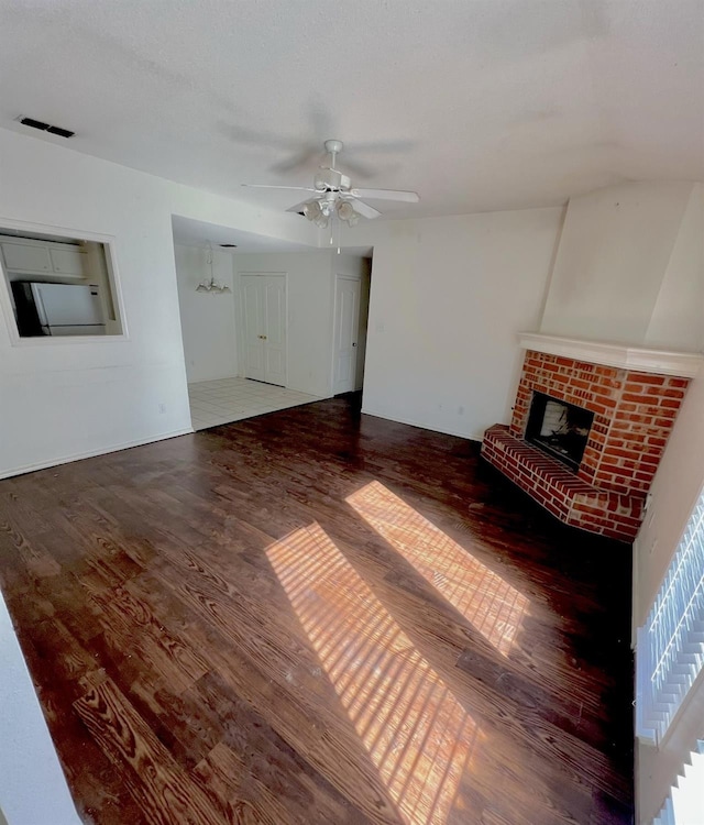 unfurnished living room featuring wood-type flooring, a brick fireplace, and ceiling fan