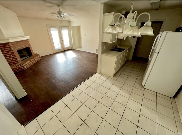 kitchen with sink, white cabinetry, white refrigerator, a fireplace, and light tile patterned flooring