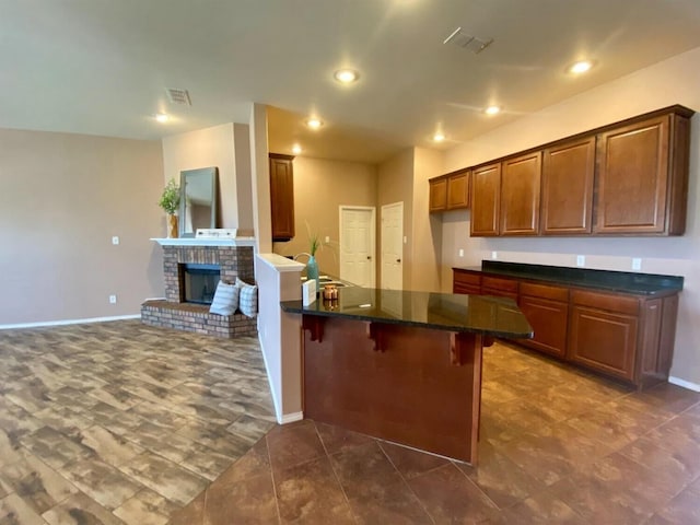 kitchen featuring dark stone counters, a kitchen breakfast bar, sink, and a brick fireplace