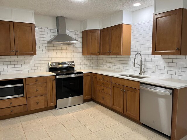 kitchen with wall chimney exhaust hood, sink, a textured ceiling, appliances with stainless steel finishes, and decorative backsplash