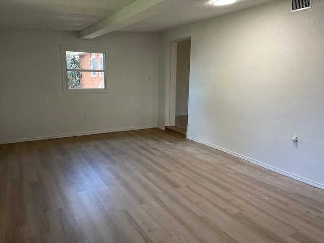 empty room with beam ceiling, light hardwood / wood-style floors, and a textured ceiling