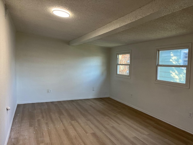 spare room with hardwood / wood-style flooring, beamed ceiling, and a textured ceiling