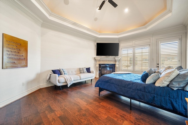 bedroom featuring baseboards, a tray ceiling, ornamental molding, hardwood / wood-style flooring, and a glass covered fireplace