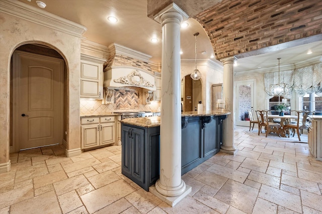 kitchen with light stone countertops, decorative columns, stone tile floors, cream cabinets, and arched walkways