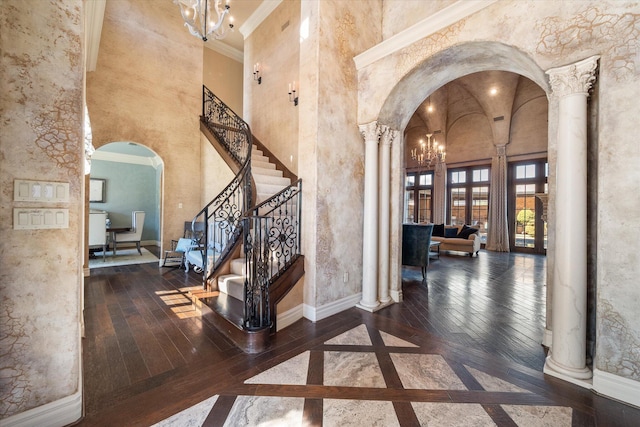 foyer entrance featuring decorative columns, arched walkways, a notable chandelier, and hardwood / wood-style flooring