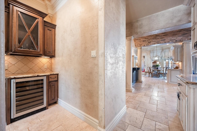 bar with baseboards, wine cooler, stone tile floors, decorative backsplash, and ornate columns