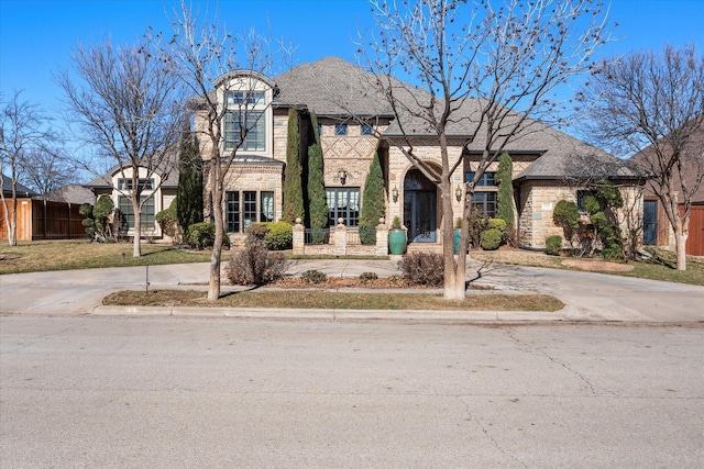 french provincial home with brick siding, fence, stone siding, and driveway