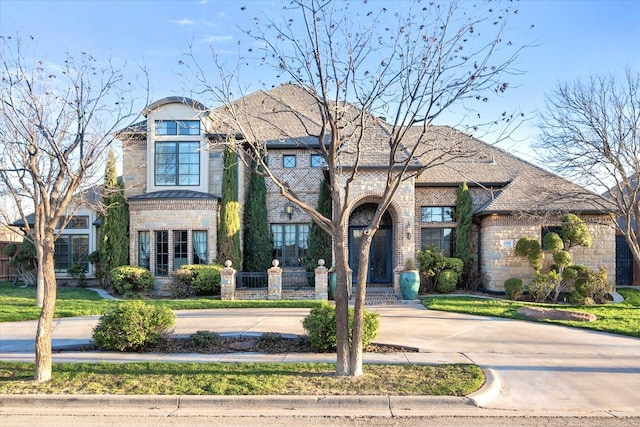 french country inspired facade with stone siding, brick siding, and a front yard