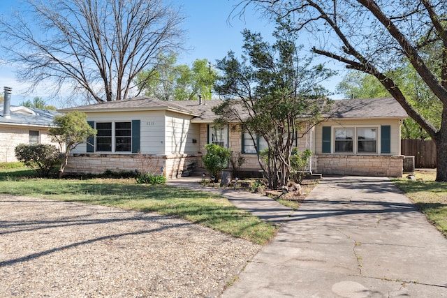 ranch-style house featuring driveway, stone siding, and fence