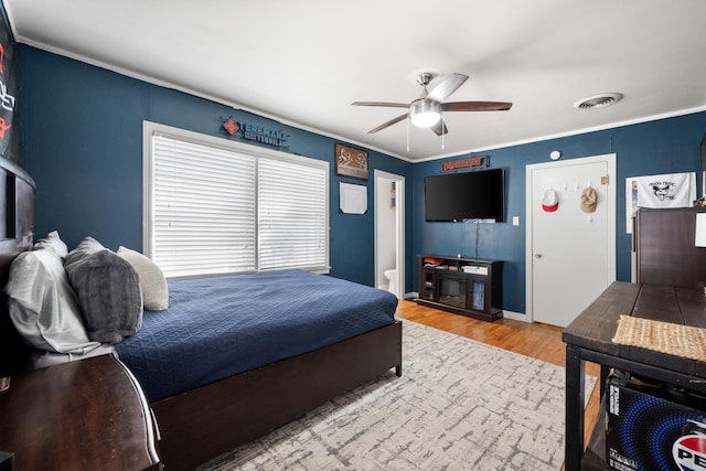 bedroom featuring ceiling fan, visible vents, baseboards, ornamental molding, and wood finished floors