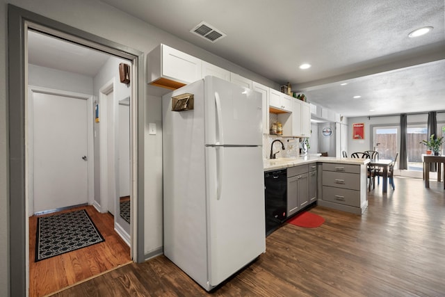 kitchen featuring freestanding refrigerator, black dishwasher, gray cabinetry, visible vents, and a peninsula