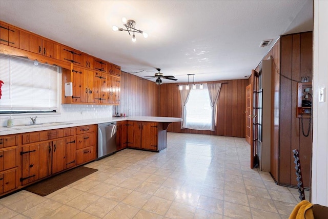 kitchen with wooden walls, decorative light fixtures, dishwasher, sink, and kitchen peninsula