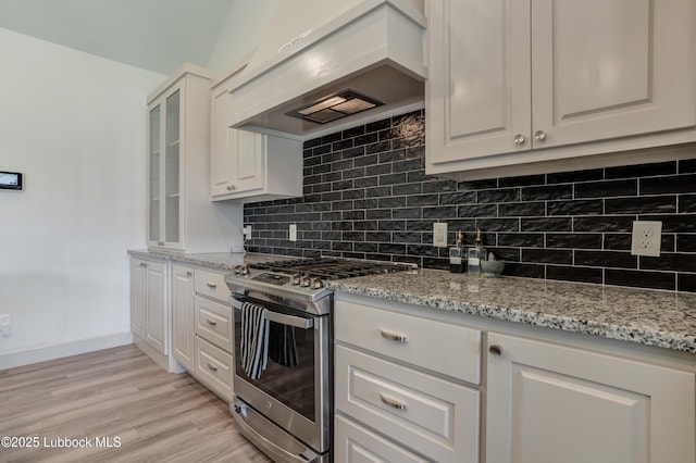 5713 116th St, Lubbock, TX 79424 - kitchen with gas range, custom exhaust hood, white cabinetry, light wood-style floors, and tasteful backsplash