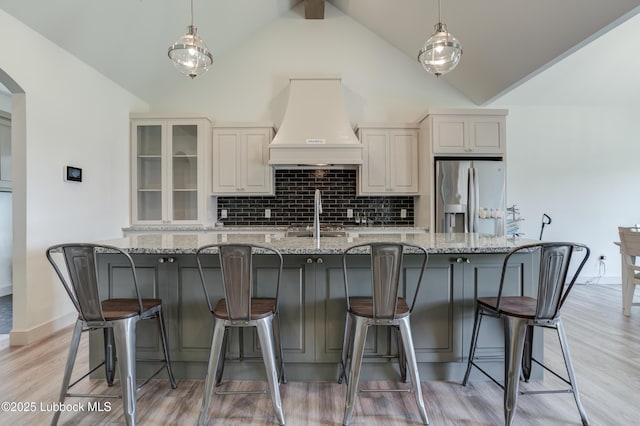 5713 116th St, Lubbock, TX 79424 - kitchen with stainless steel refrigerator with ice dispenser, custom exhaust hood, light stone countertops, tasteful backsplash, and light wood-style flooring