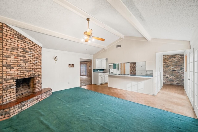 unfurnished living room with a fireplace, lofted ceiling with beams, ceiling fan, light carpet, and a textured ceiling