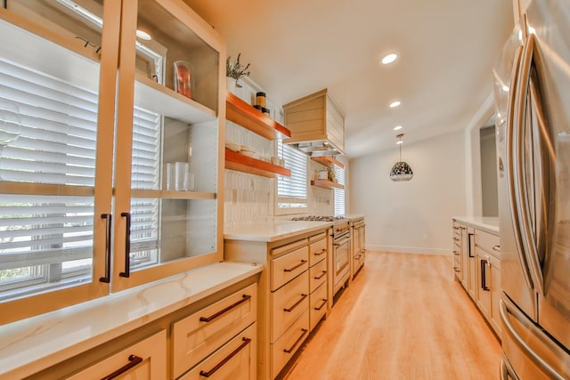 kitchen with appliances with stainless steel finishes, pendant lighting, light brown cabinets, and light hardwood / wood-style flooring