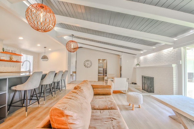 living room with a brick fireplace, vaulted ceiling with beams, wood ceiling, and light wood-type flooring